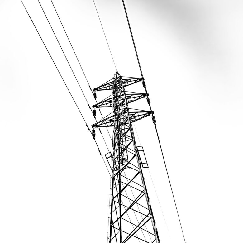 A monotone phone from the ground looking up at high voltage power lines with a cloudy sky above.