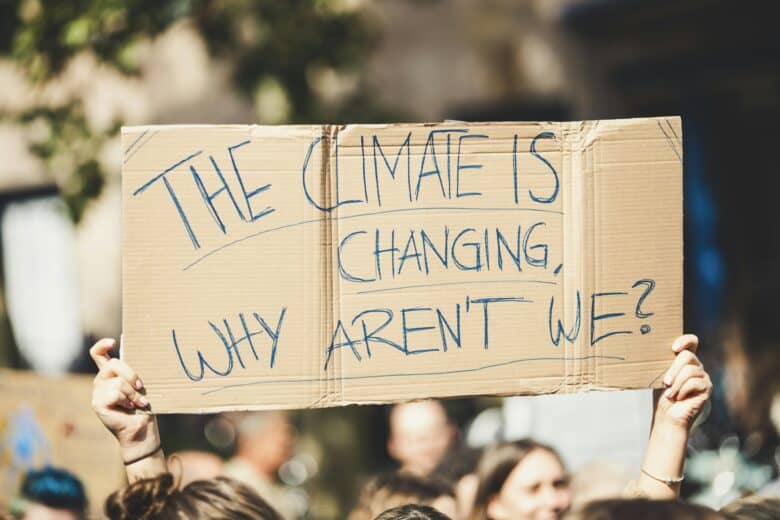 People in a crowd rally holding a cardboard sign with the handwriting saying 'The climate is changing, why aren't we?'